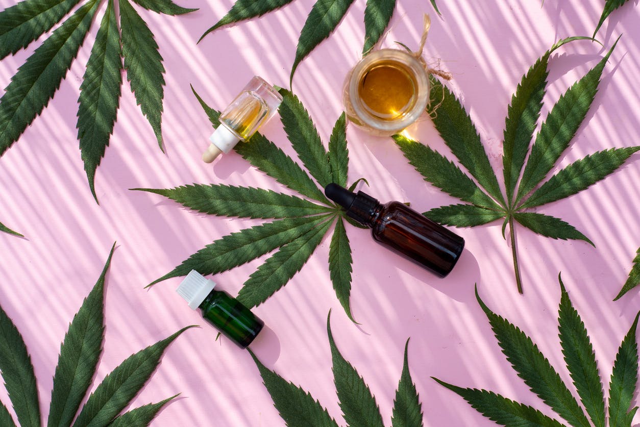 Marijuana industrial cannabis hemp leaves and products like oil, cream and tincture flat lay pattern on pink background top view