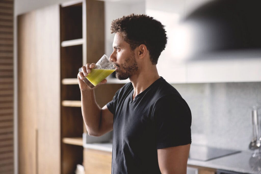 Fit African American man drinking a green juice for breakfast at home - healthy lifestyle concepts