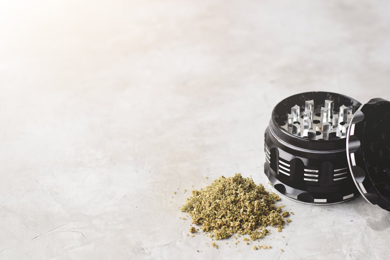 Cannabis grinder with ground weed on grey background with copy space