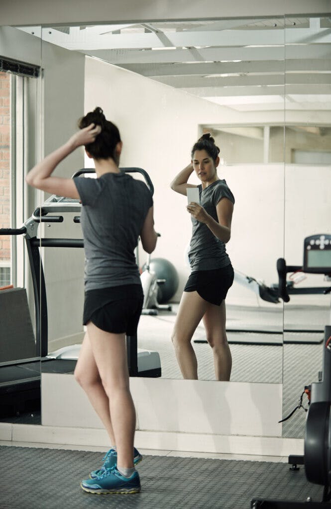 Shot of a young woman taking pictures of herself in the mirror with her cellphone at a gym indoors