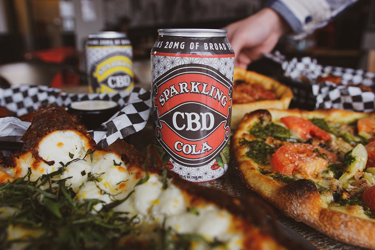 sparkling CBD soda can sitting on a table surrounded by pizza and Italian food