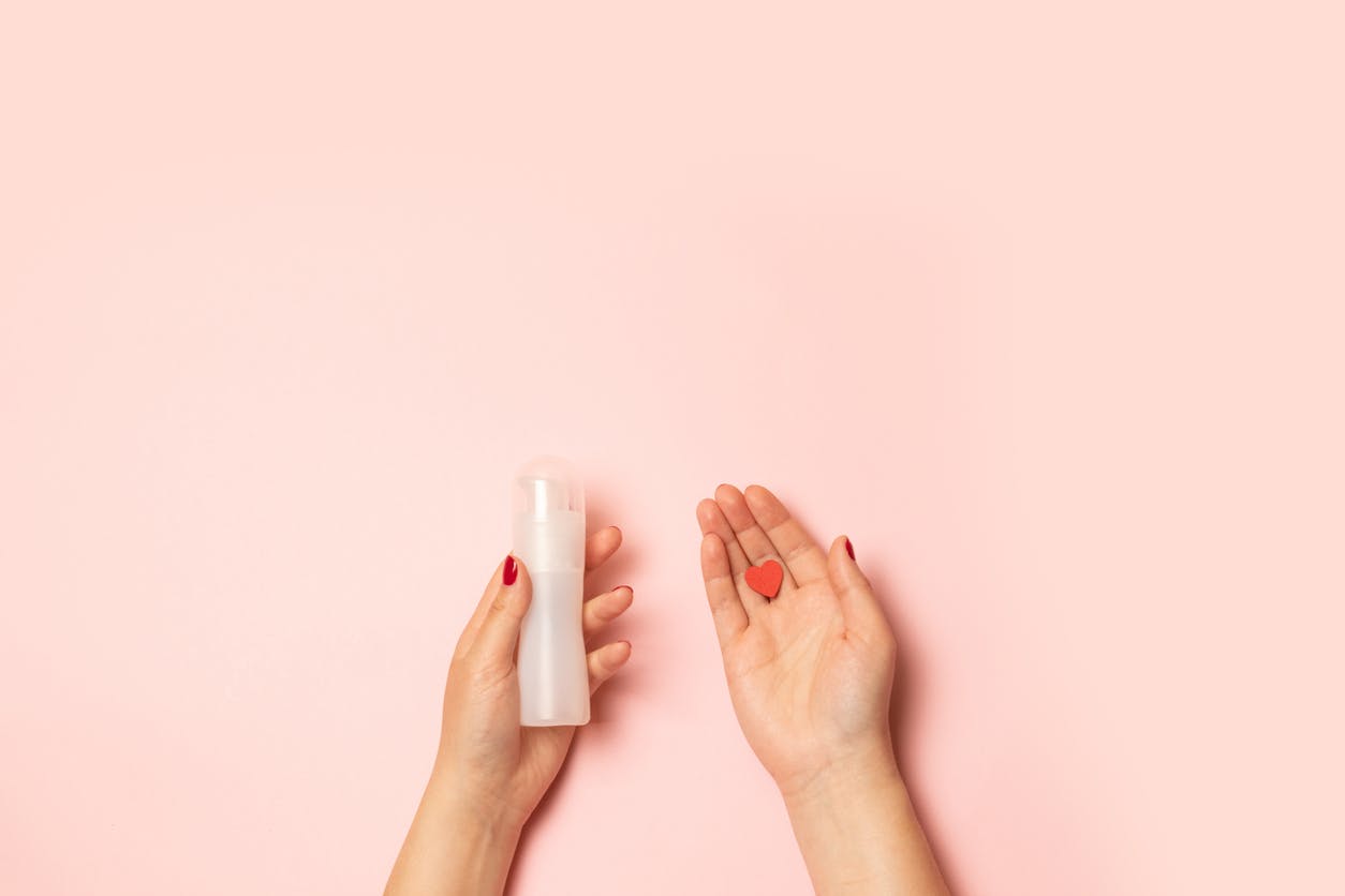 Womens hands hold cannabis lube and a red heart shape on a pink background