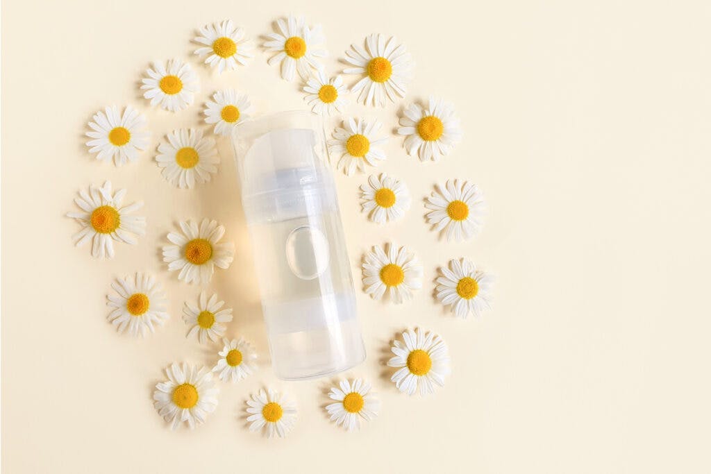 Transparent bottle of intimate lubricant gel and daisy flowers on yellow background. Intimate massage and comfortable sex consept. Top view, mockup, template.