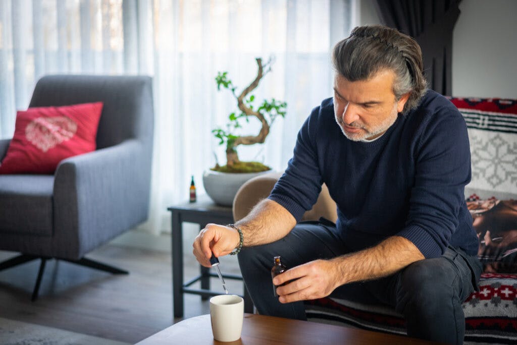 Sick man adding CBD oil to morning tea at home