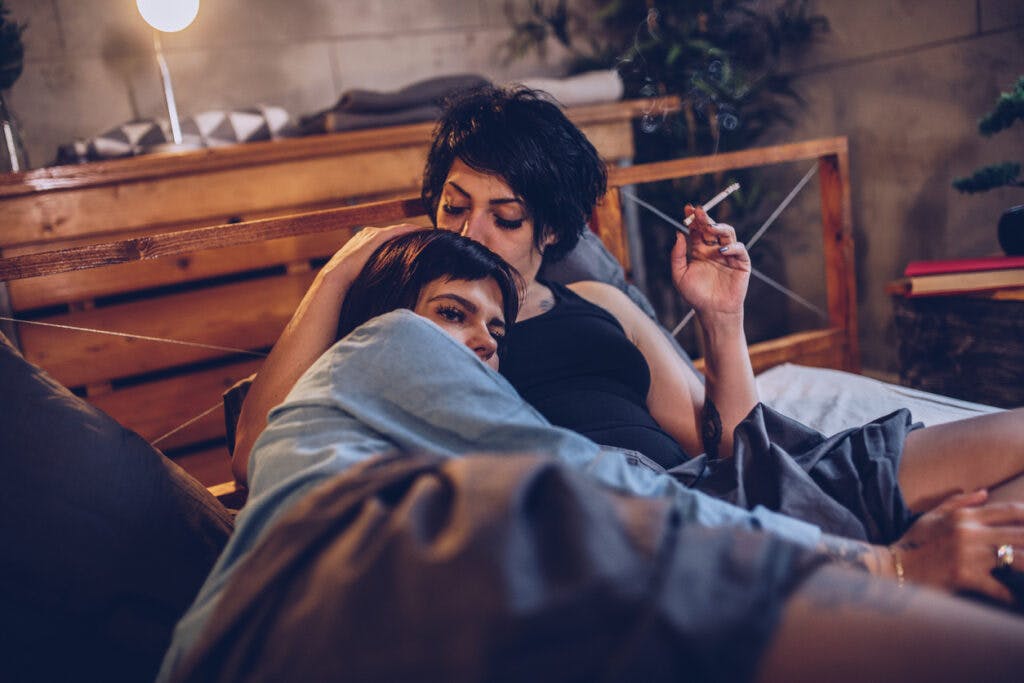 Female couple lying in the bed and smoking cigarette