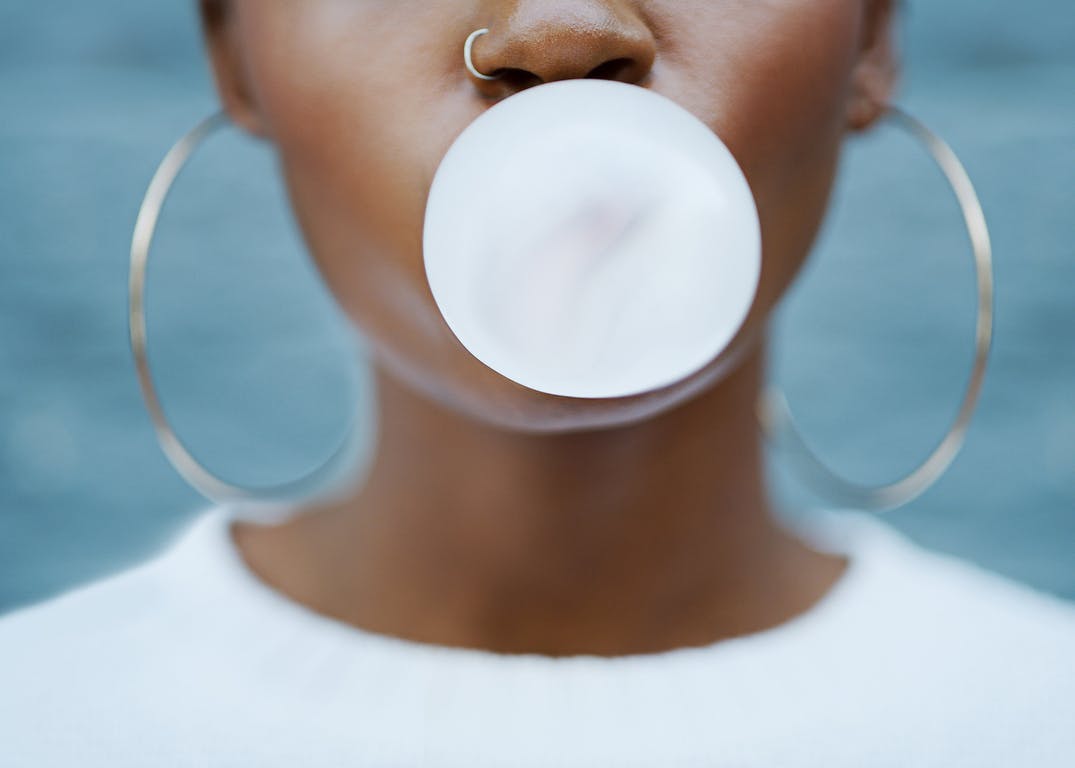 Shot of an unrecognizable woman blowing a bubble with her gum against a grey background outdoors