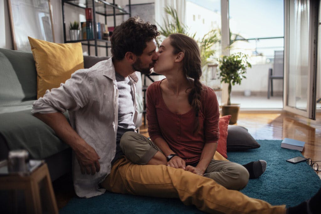 Young couple kissing while sitting on their living room floor