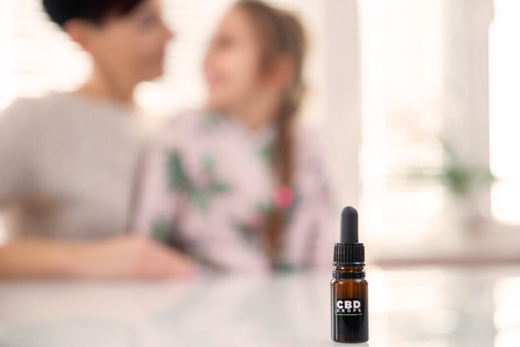 CBD Oil Bottle on Table With Mother and Daughter in Background.