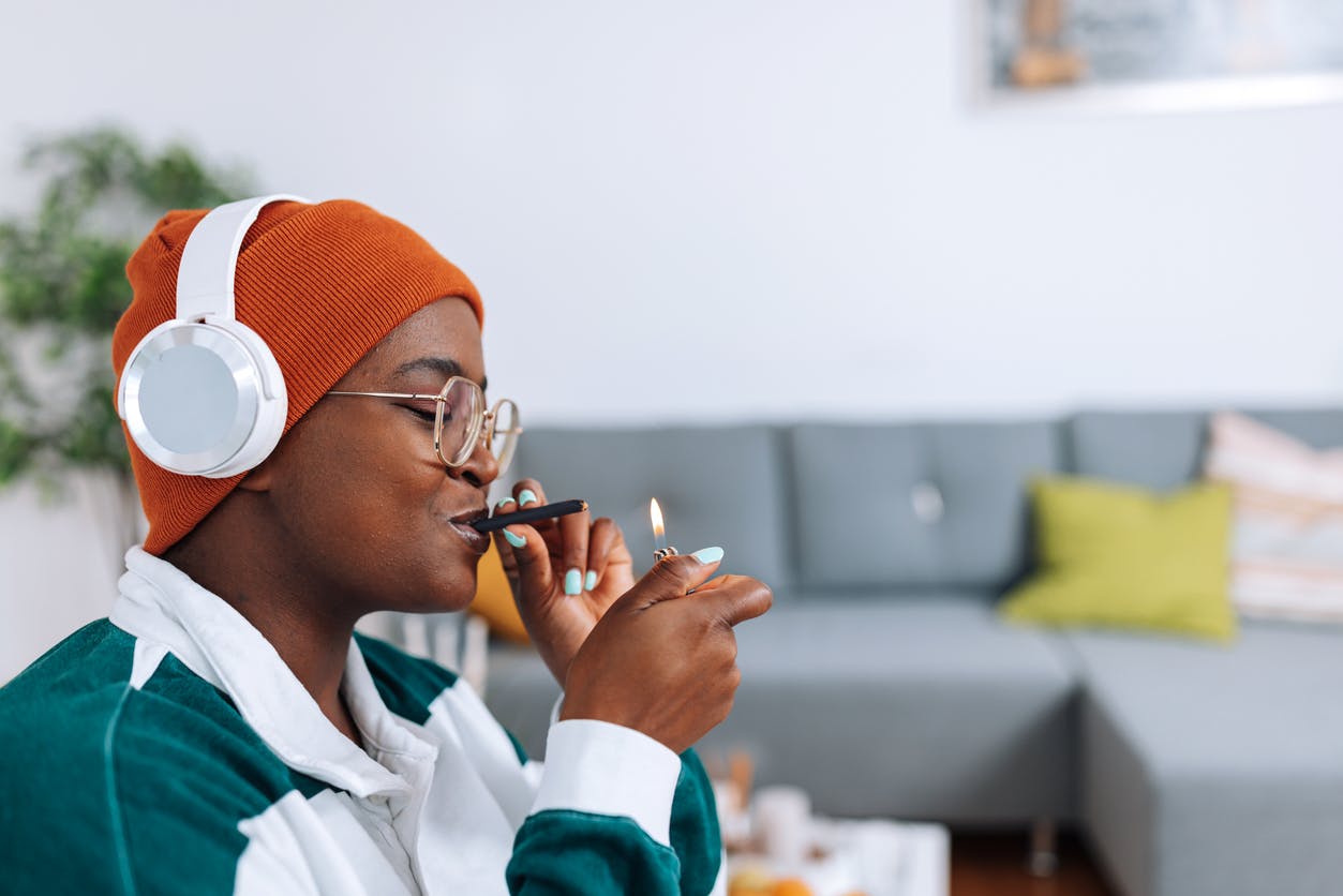 A young African American woman in a wheelchair combines the therapeutic benefits of CBD and music therapy as she smokes a legal joint and listens to her favorite tunes through her headphones