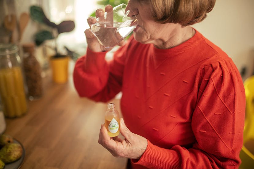 Senior woman drinks a glass of water with cannabis oil, which is good for relieving stress symptoms