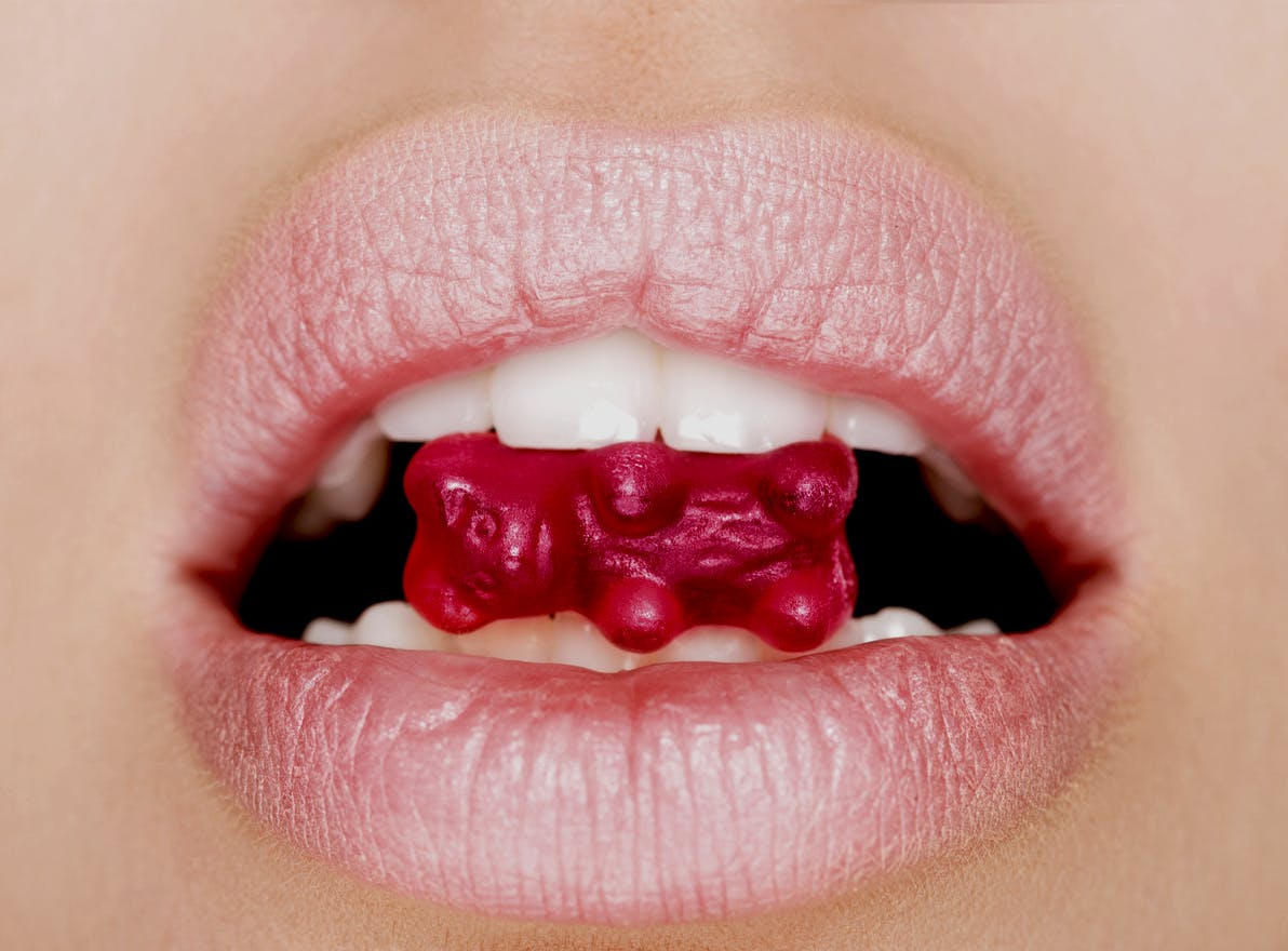 Close up of female perfectly white healthy teeth biting gummy bear candy. Concept of CBD gummies for sex