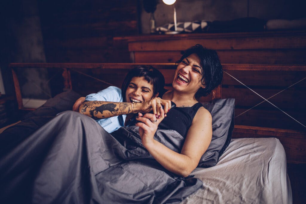 Two girls, young lesbian couple relaxing together at home in bed, watching television.