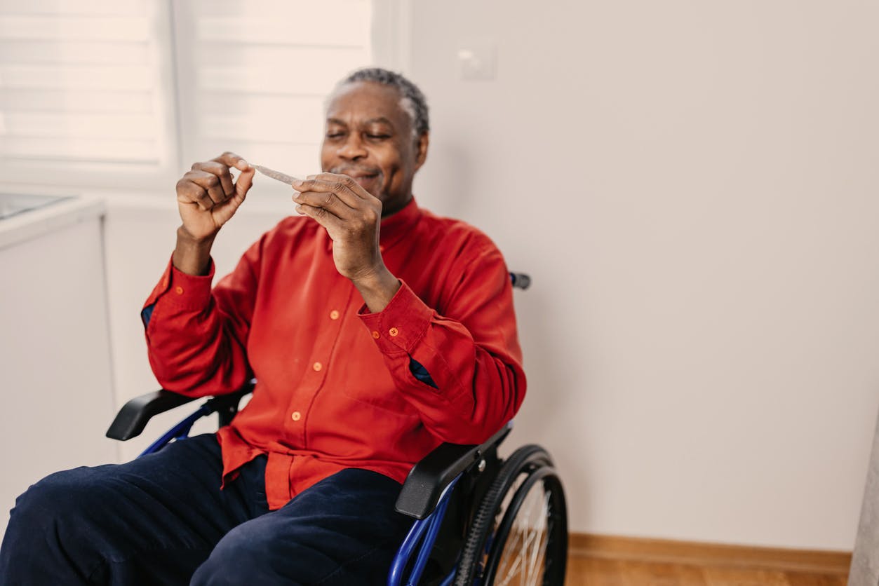A senior African-American man in a wheelchair is smiling while holding a CBD joint and a lighter.